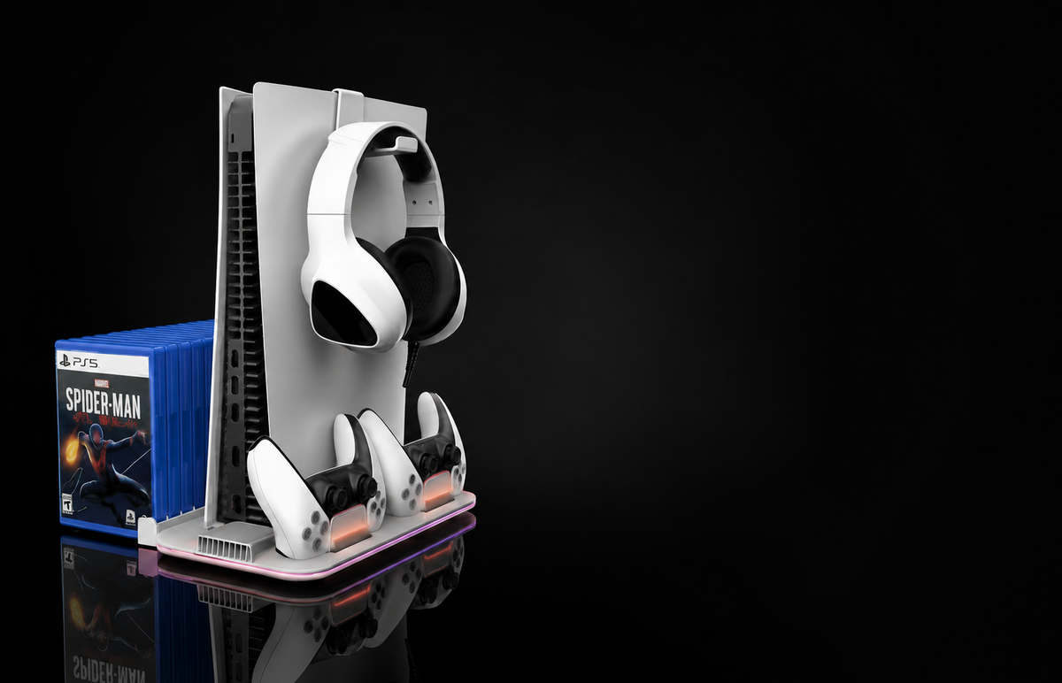 A PlayStation 5 console on a white vertical stand with attached controllers, white over-ear headphones, and two game cases, photographed on a black reflective studio background.